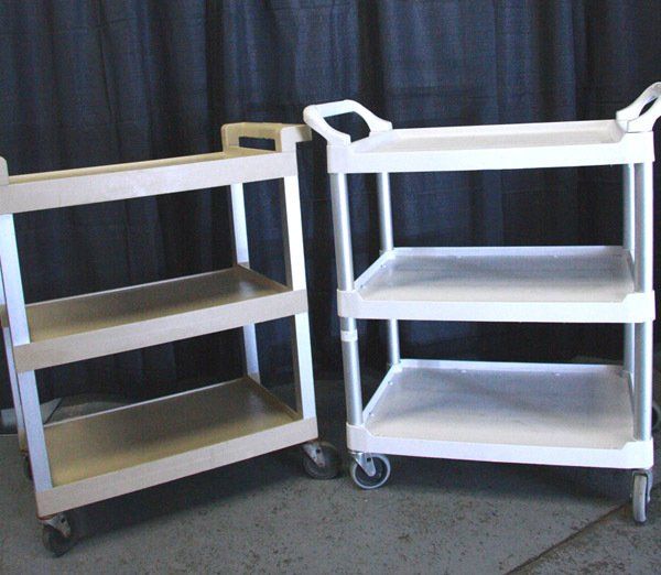 Two white utility carts on wheels beside a beige cart against a dark curtain backdrop