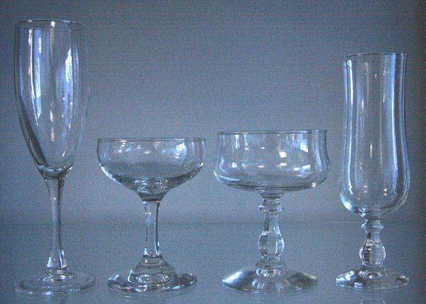 Four clear glass stemware pieces on a gray surface, including a champagne flute and three goblets.