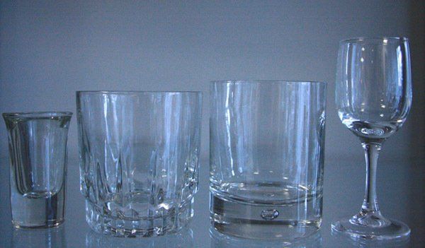 Four clear drinking glasses of different shapes lined up on a blue surface