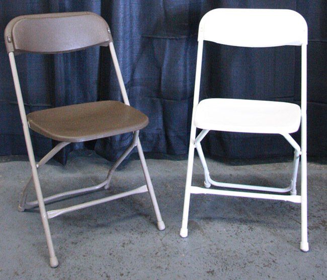 Two folding chairs, one brown and one white, standing side by side on a concrete floor.