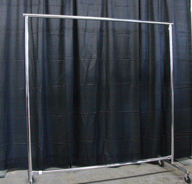 Freestanding metal garment rack on wheels against a black curtain backdrop