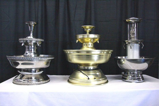 Three decorative silver and gold tiered fountains on a white table against a dark curtain backdrop