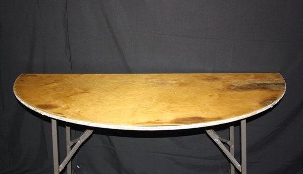 Oval wooden table with metal folding legs against a dark backdrop