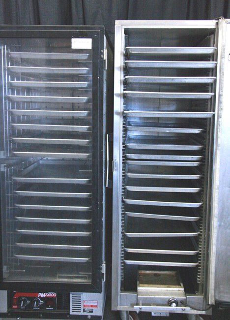 Two stainless steel industrial racks with many horizontal shelves, one partly open, in a factory setting