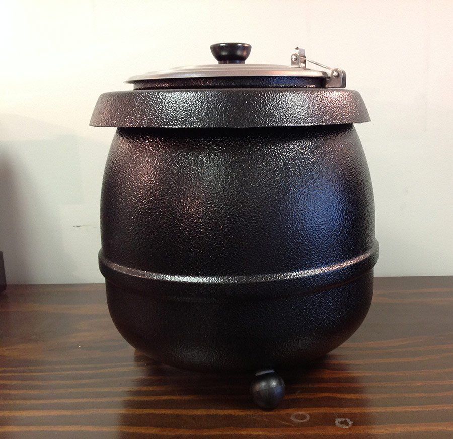 Black lidded pot on a wooden table against a plain wall.