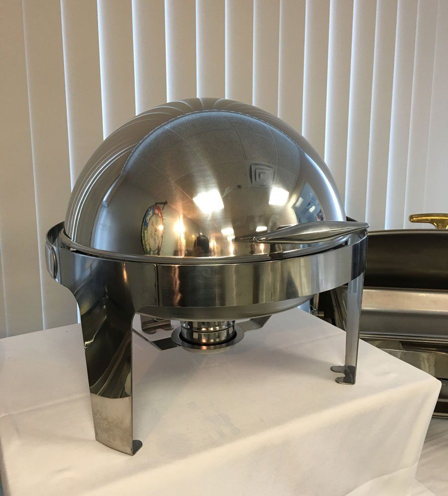 Chrome domed chafing dish on a white table in front of vertical blinds