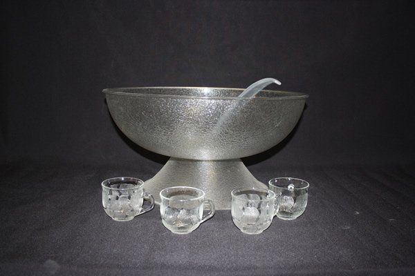 Silver bowl with a curved spout, surrounded by four small clear cups on a dark background