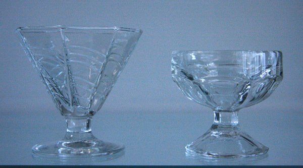 Two clear glass dessert dishes on a blue surface, one tall and fluted, one short and wide