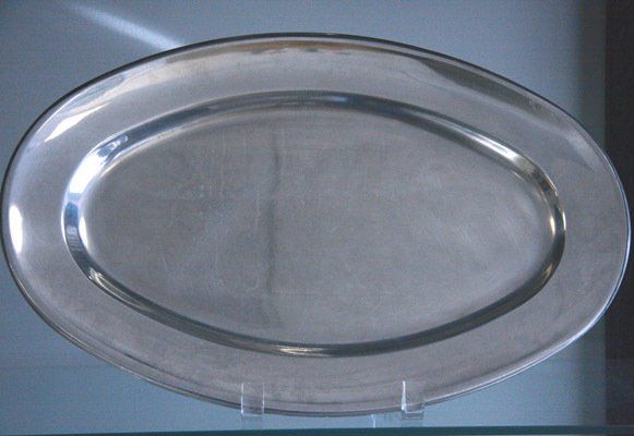 Oval silver serving tray on a clear stand against a light background