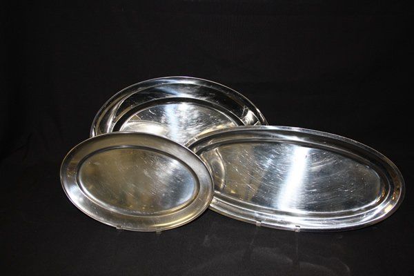 Three shiny silver serving trays on a black background