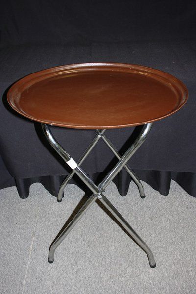 Round brown tray table with folded chrome legs against a black curtain background
