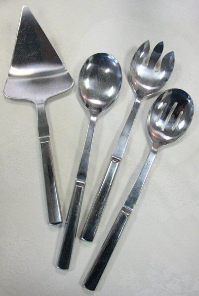 Four stainless steel serving utensils on a light fabric background