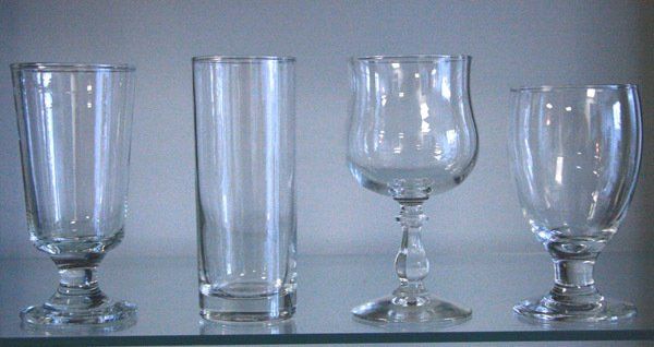 Four clear glass goblets and tumblers lined up on a shelf against a gray background
