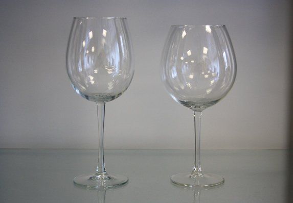Two clear wine glasses on a reflective surface against a plain gray background