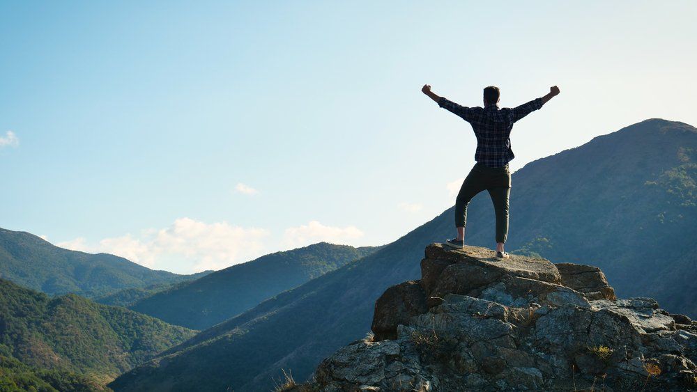 On the edge of a rocky cliff a man raises his hands to heaven as a sign of freedom or victory and in