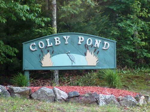 A sign for colby pond is surrounded by rocks and trees