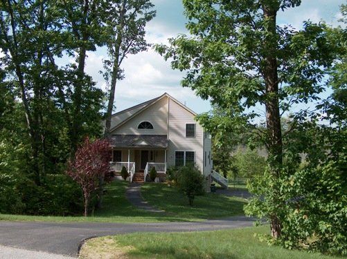 A white house with a porch is surrounded by trees