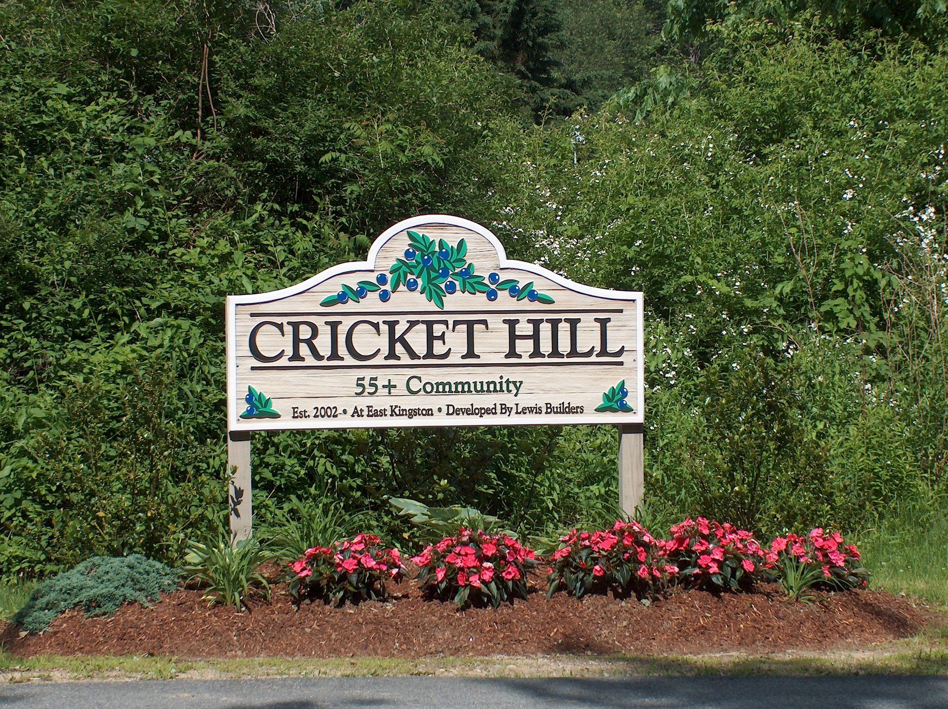 A sign for cricket hill is surrounded by trees and flowers
