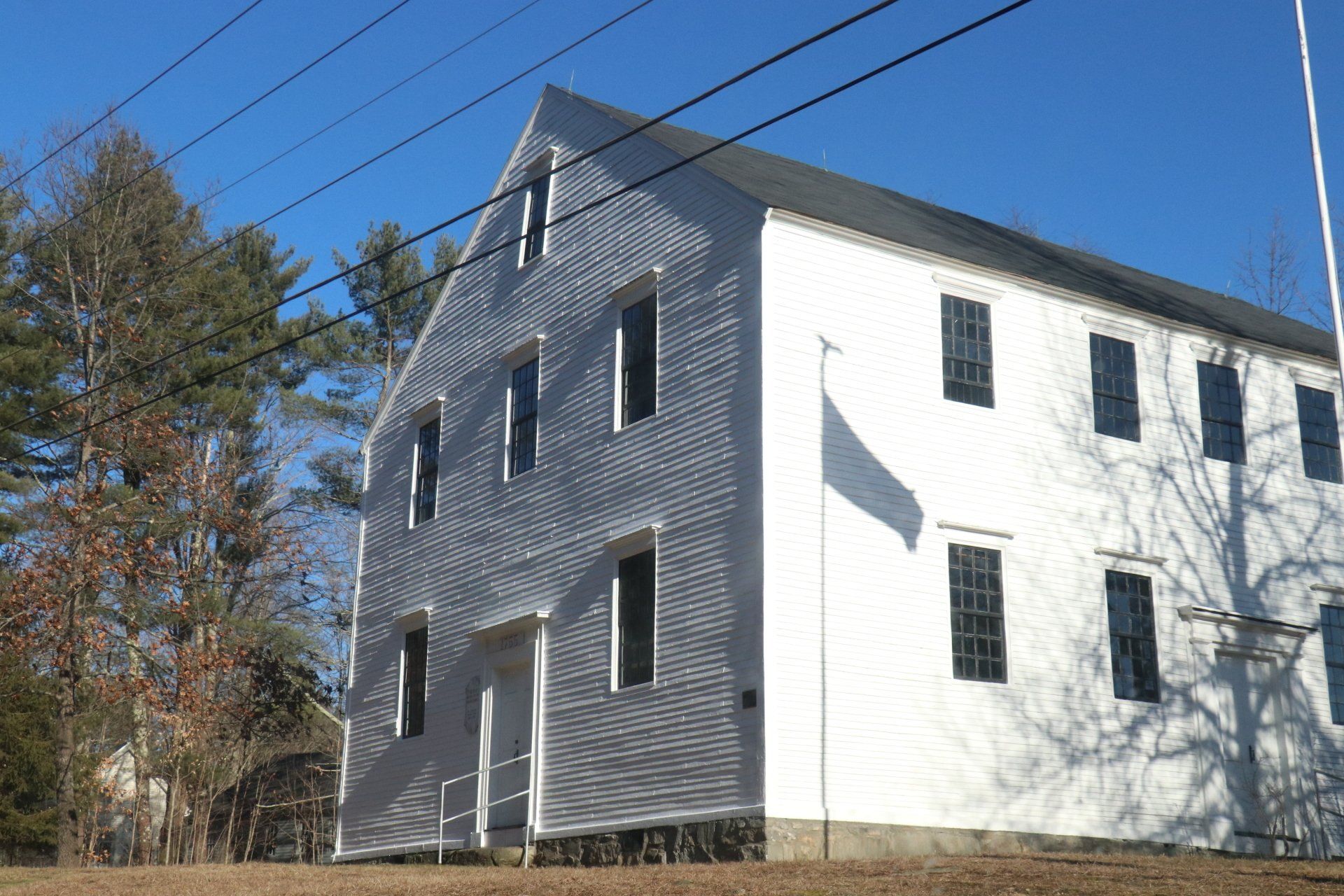 A large white building with black windows is surrounded by trees and power lines