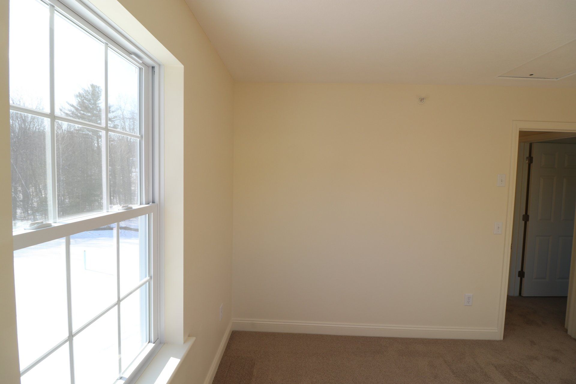 An empty room with a large window and a carpeted floor.