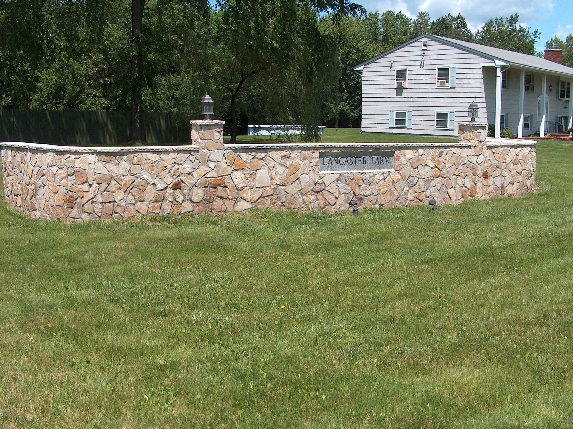 A stone wall in a grassy field with a house in the background