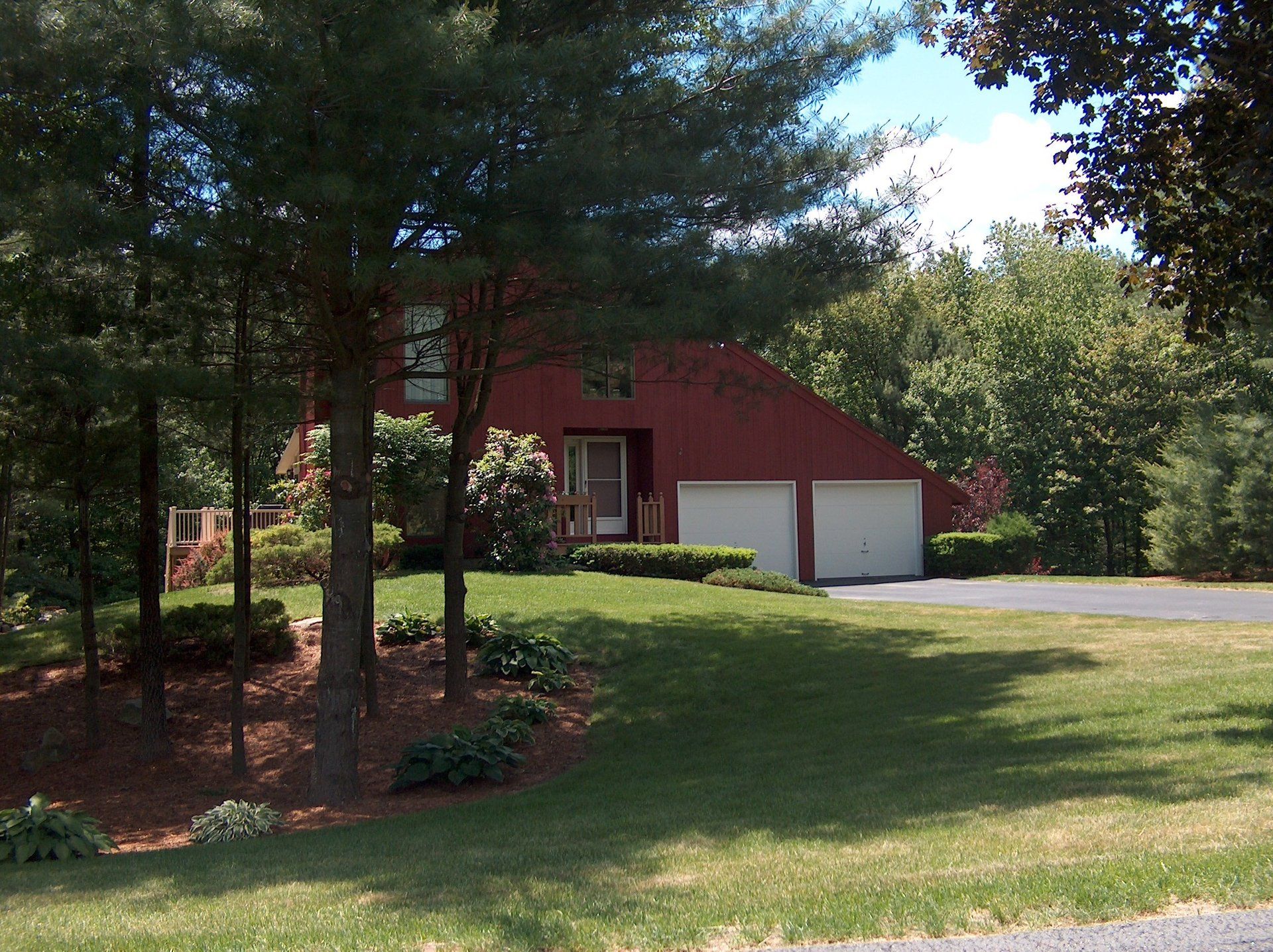 A red house with a white garage is surrounded by trees