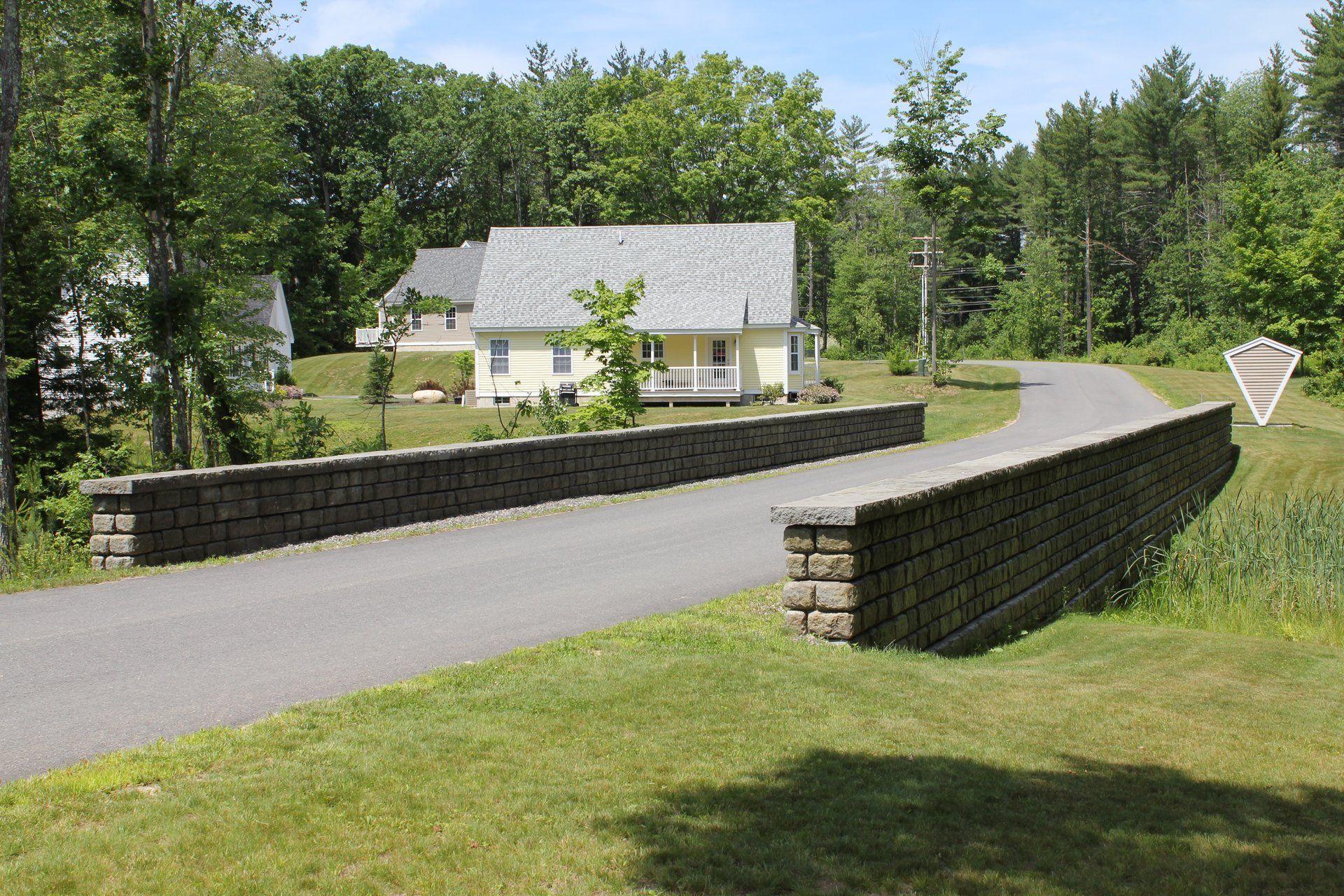 A brick wall along the side of a road leads to a house