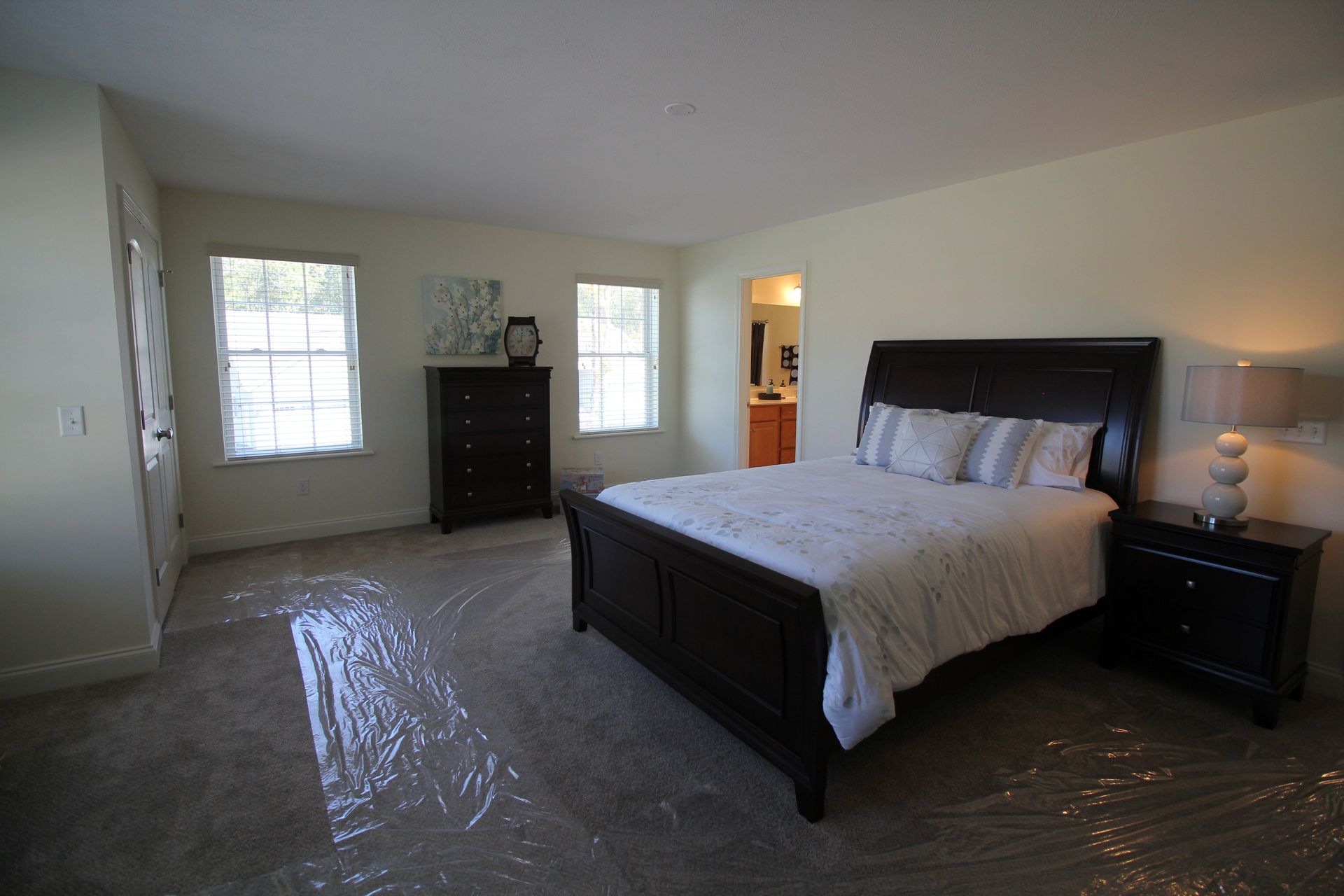 A bedroom with a bed , nightstand , dresser and two windows.