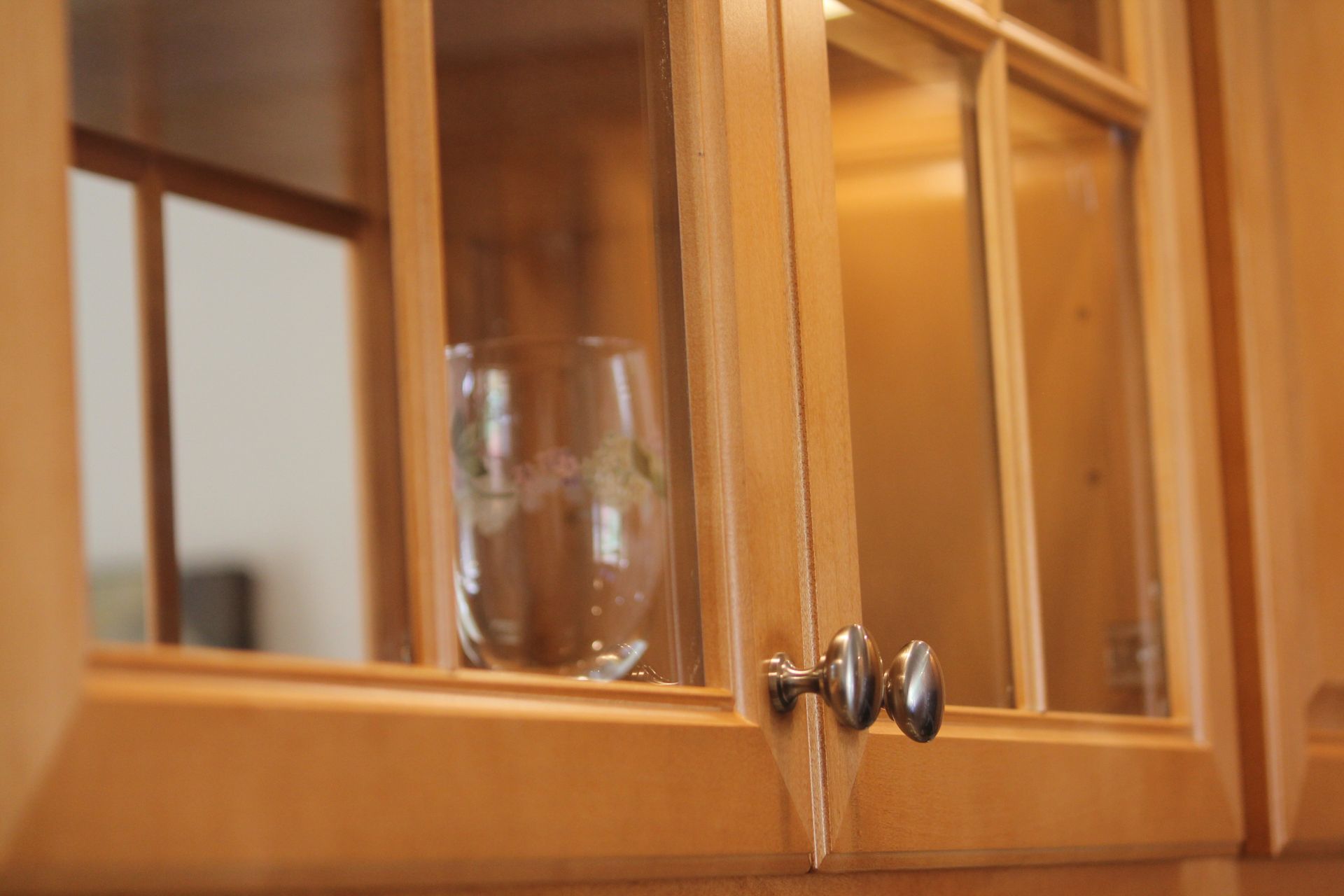 A wine glass is sitting in a glass cabinet in a kitchen.