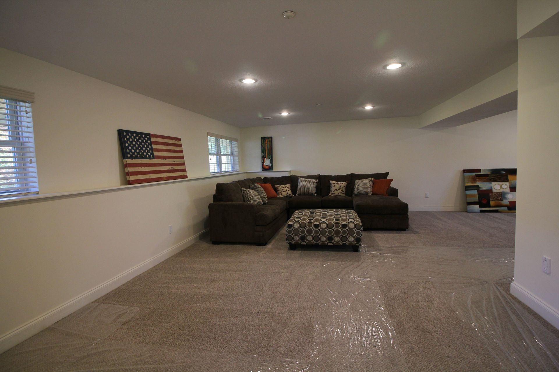 A living room with a couch , ottoman , and american flag on the wall.