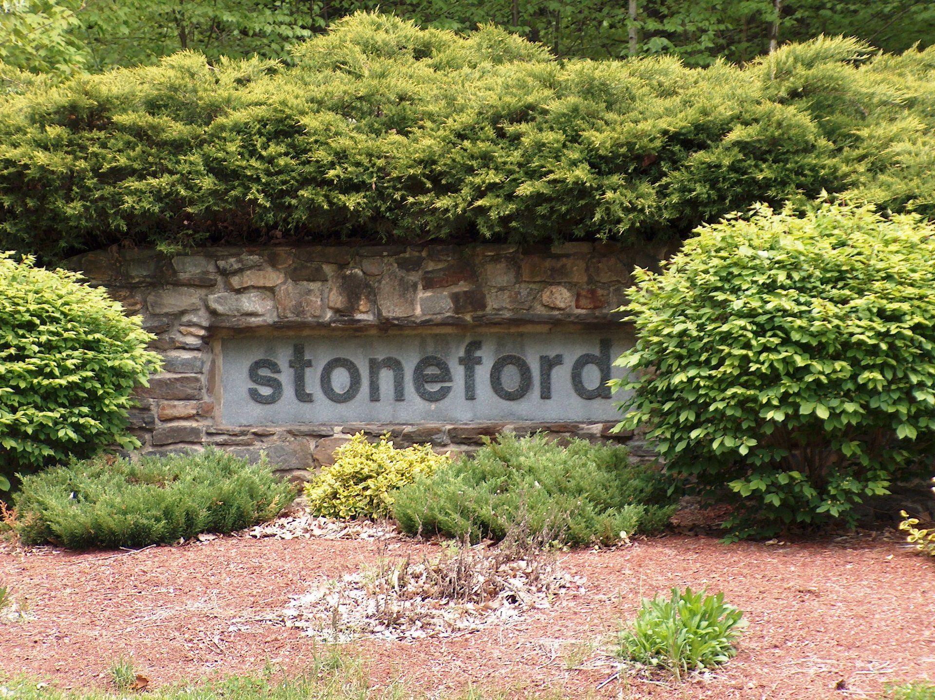 A stone sign for stoneford is surrounded by bushes and gravel