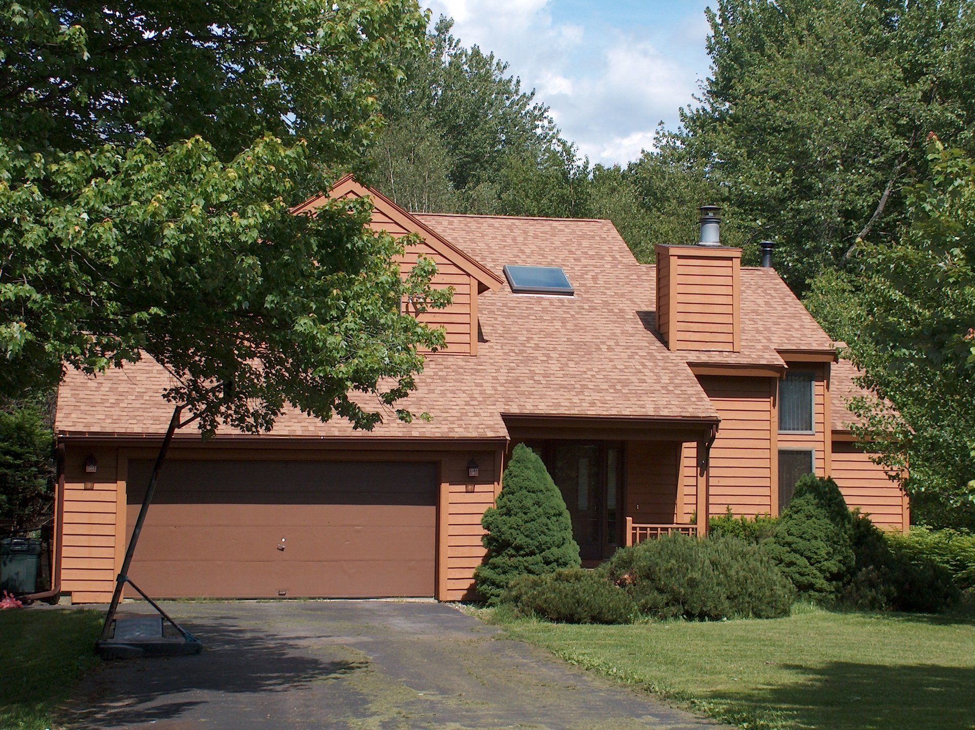 A house with a brown garage door is surrounded by trees