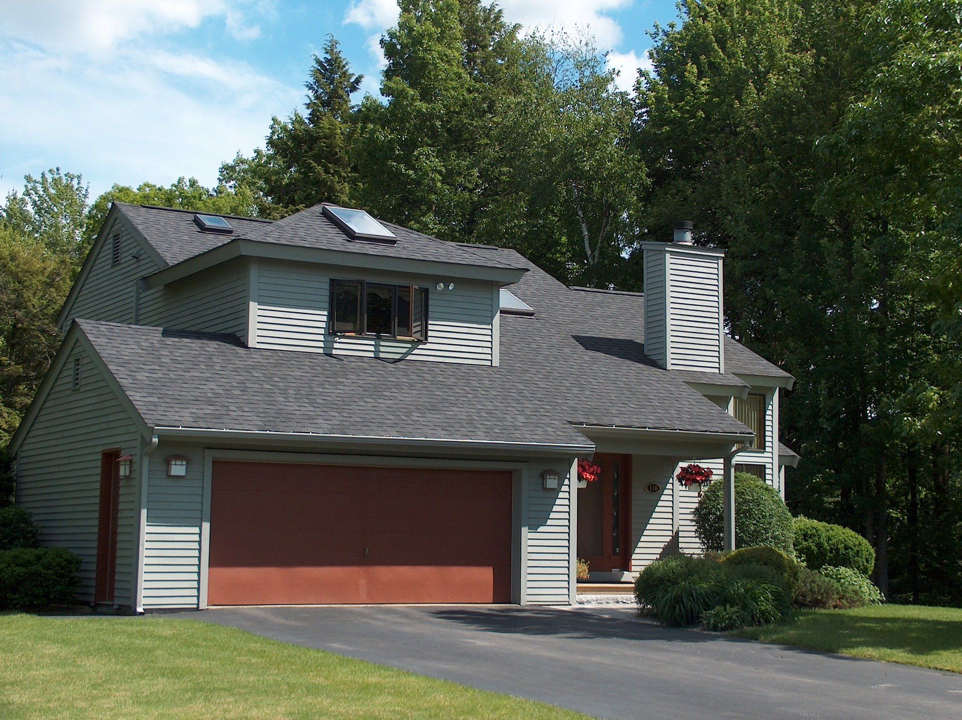 A house with a red garage door is surrounded by trees