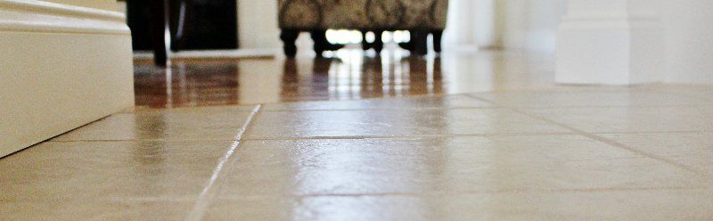 A tiled floor in a hallway with a chair in the background.