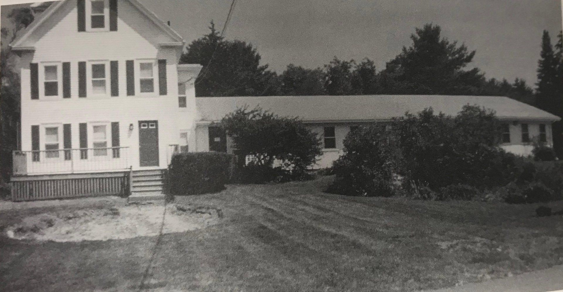 A black and white photo of a large white house surrounded by trees.