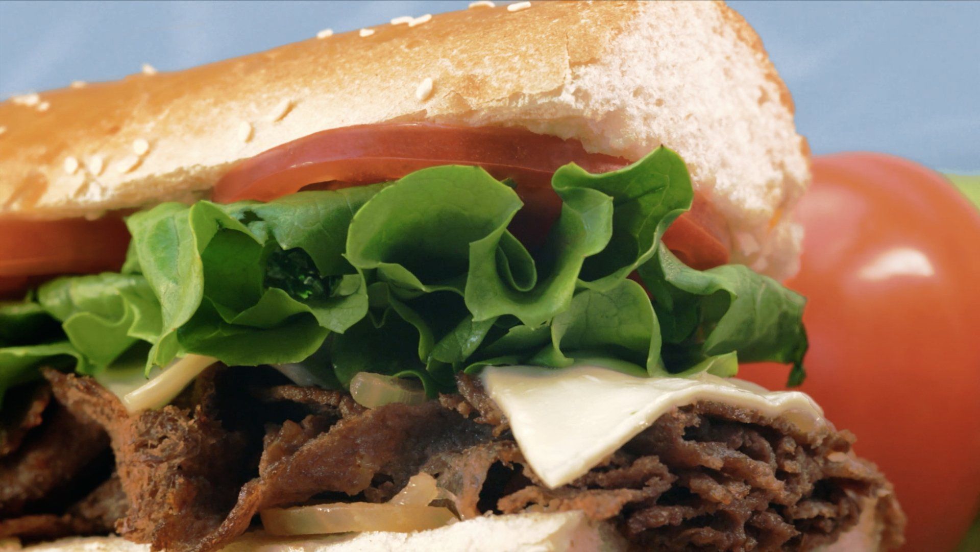 A sandwich with beef , lettuce , tomatoes and cheese on a bun.