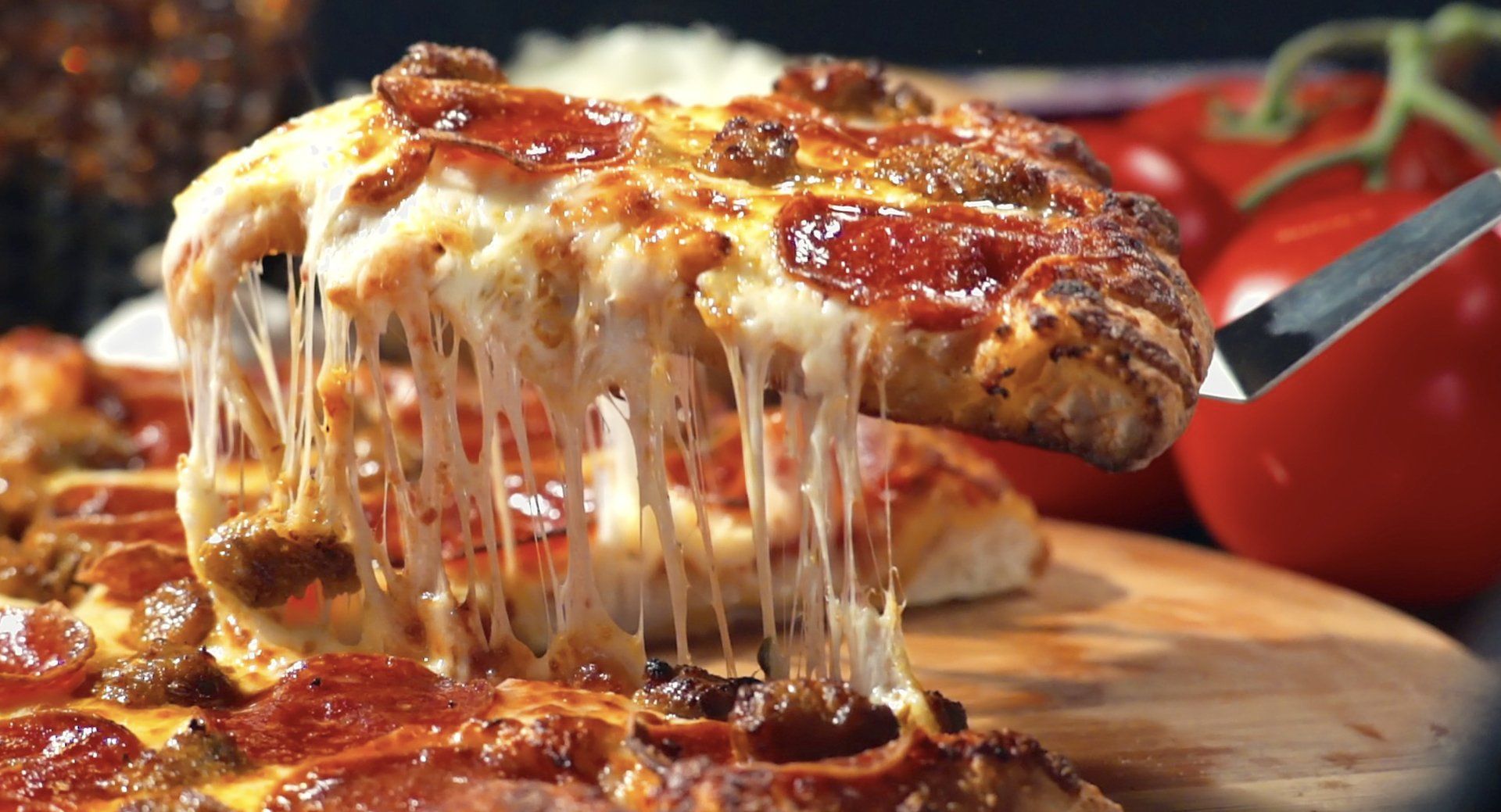 A slice of pepperoni pizza is being taken out of a pizza on a cutting board.