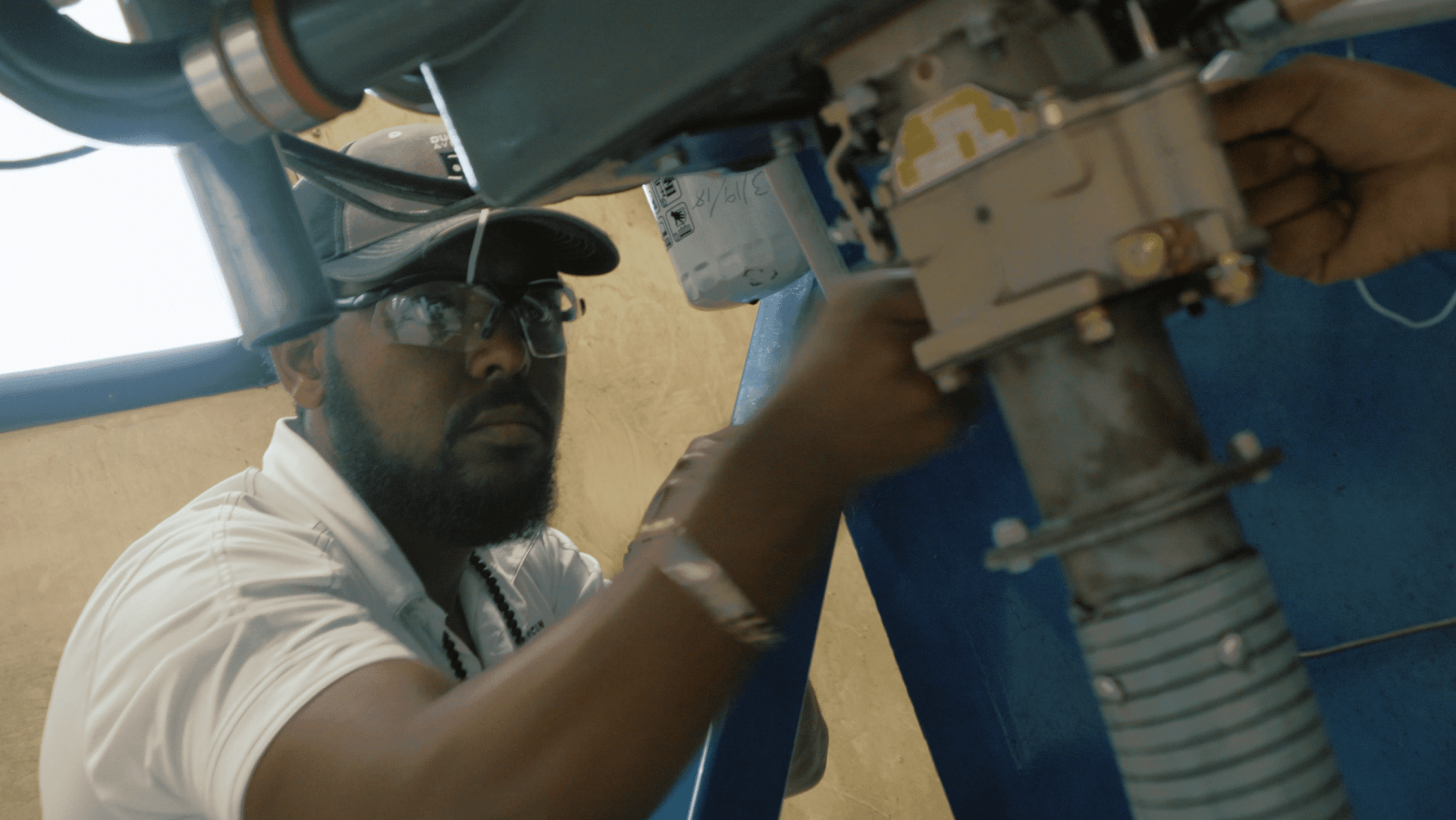 A man wearing a hat and glasses is working on a machine.