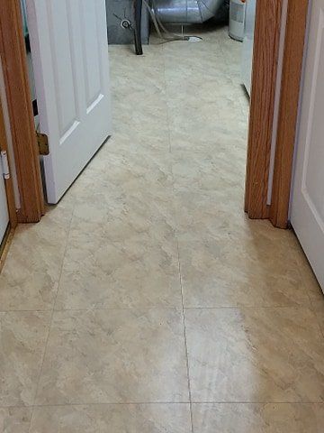 A hallway with tile floors and wooden doors leading to a bathroom.