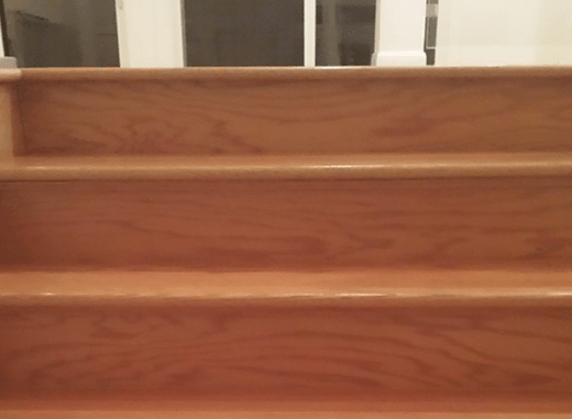 A close up of a wooden staircase with a railing in the background.