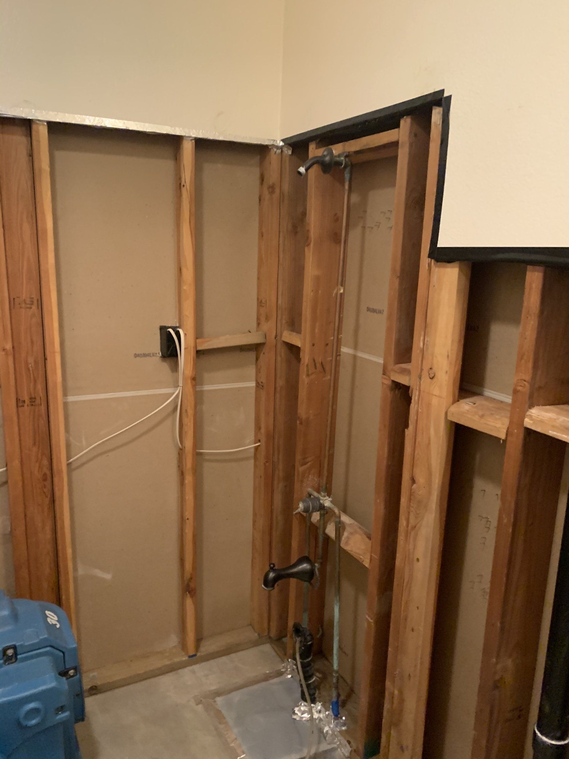 Unfinished bathroom wall studs exposed, with plumbing pipes and a shower valve visible.