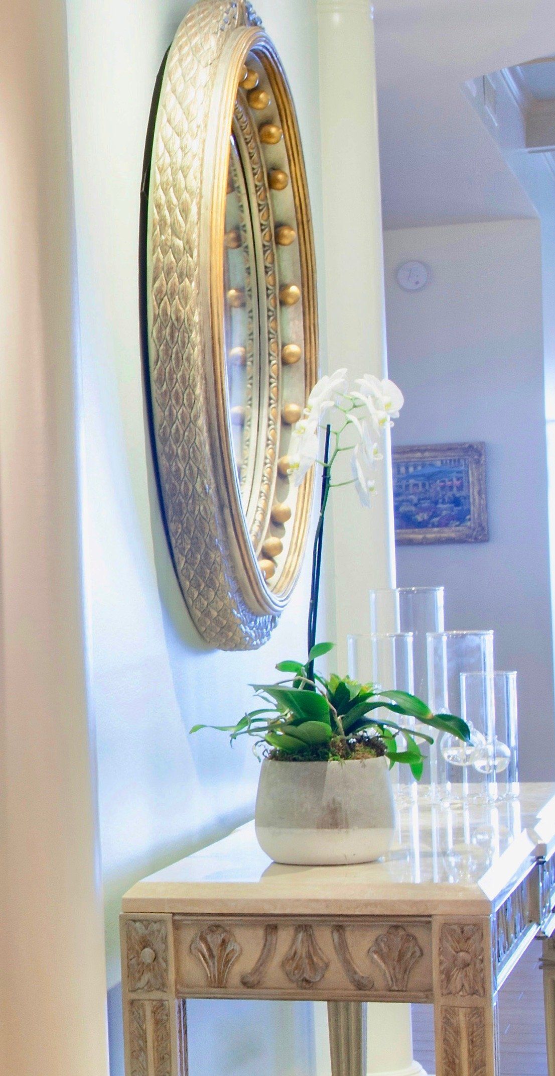 Ornate gold mirror above a small table with a white orchid in a bright hallway