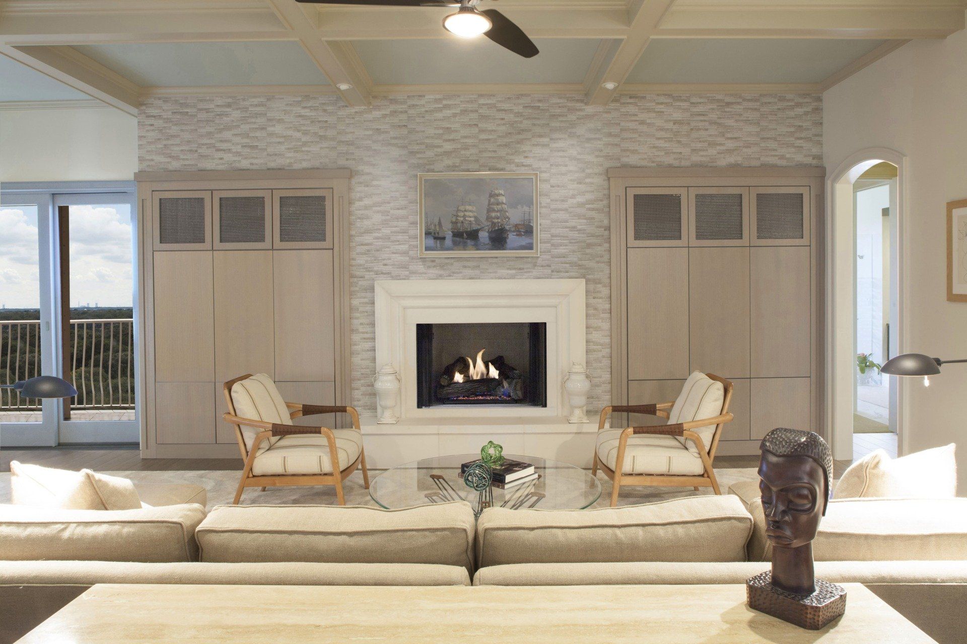 Bright living room with a central fireplace, beige sofas, and French doors leading outside.