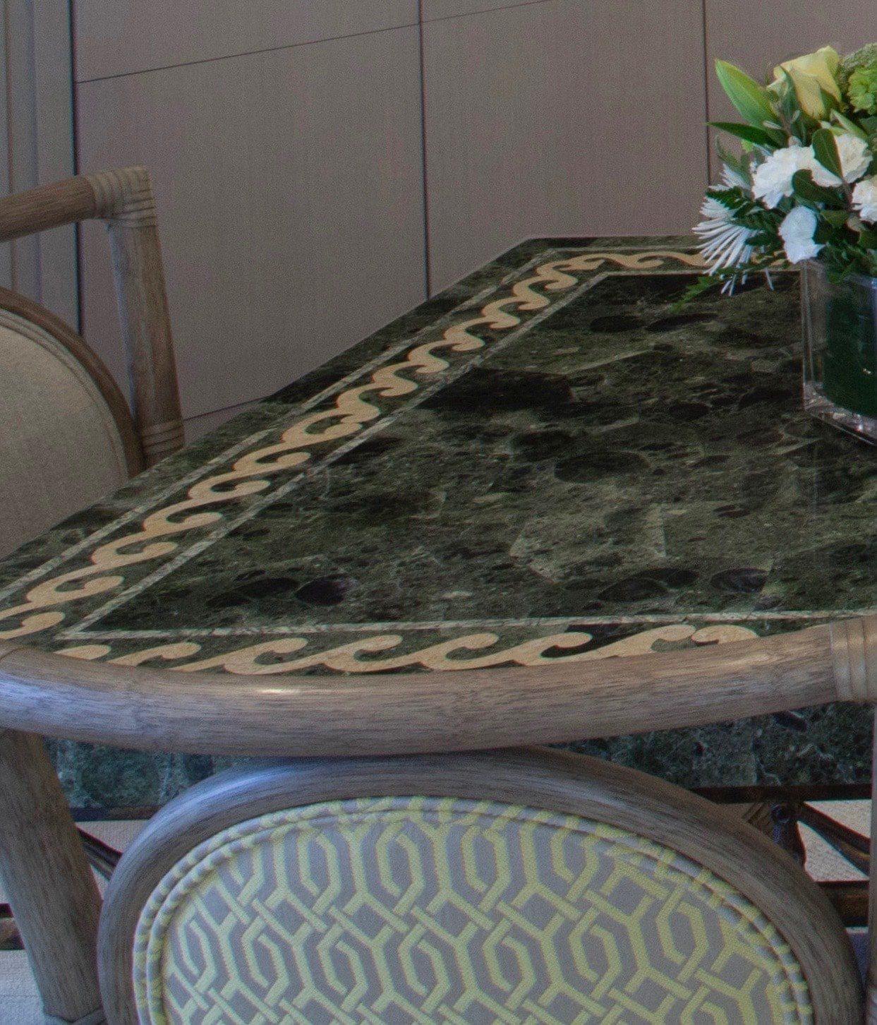 Small round marble-top table with upholstered chairs and a vase of flowers in a dining room.