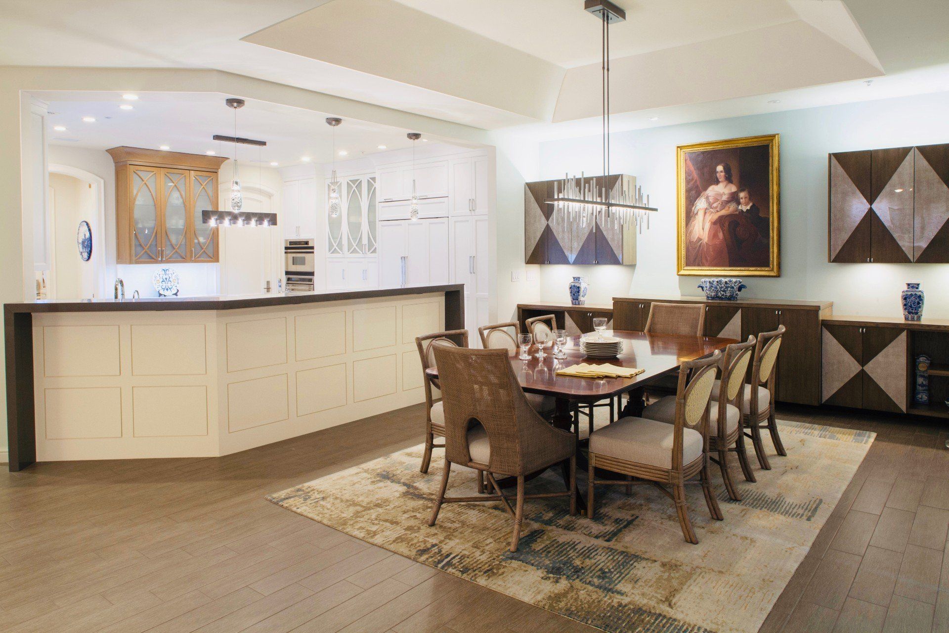 Bright dining room with a large table, upholstered chairs, and a kitchen counter in the background.