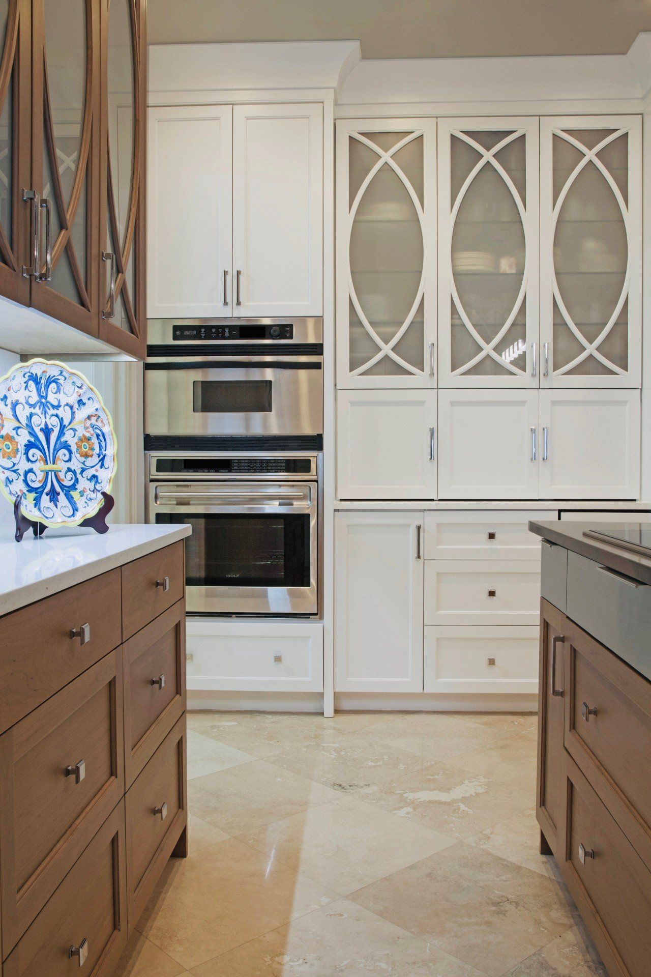 Bright kitchen with white cabinets, built-in ovens, and brown lower drawers; decorative plate on the counter.