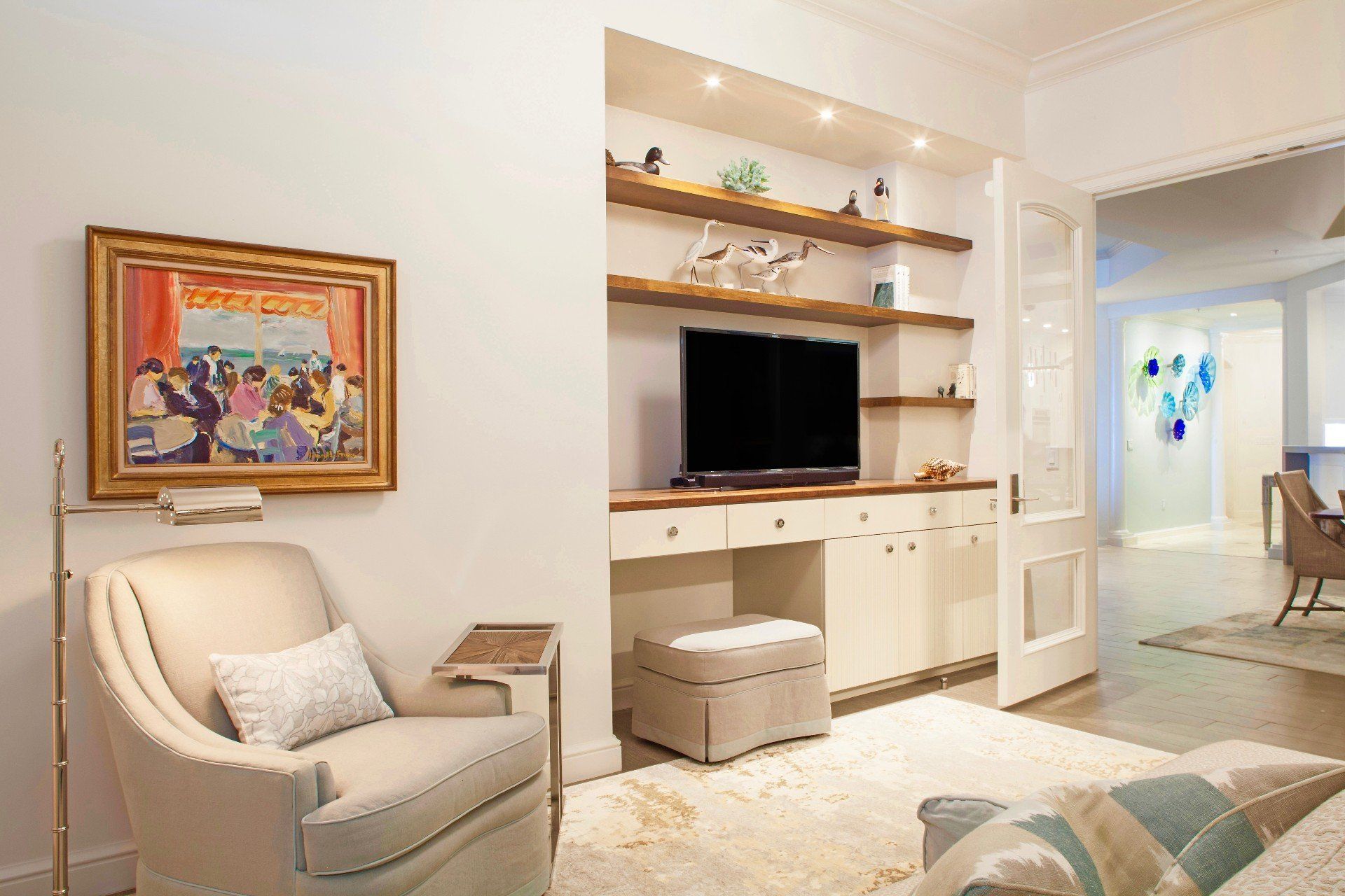 Bright modern living room with white armchair, TV, built-in shelves, and open doorway to dining area.