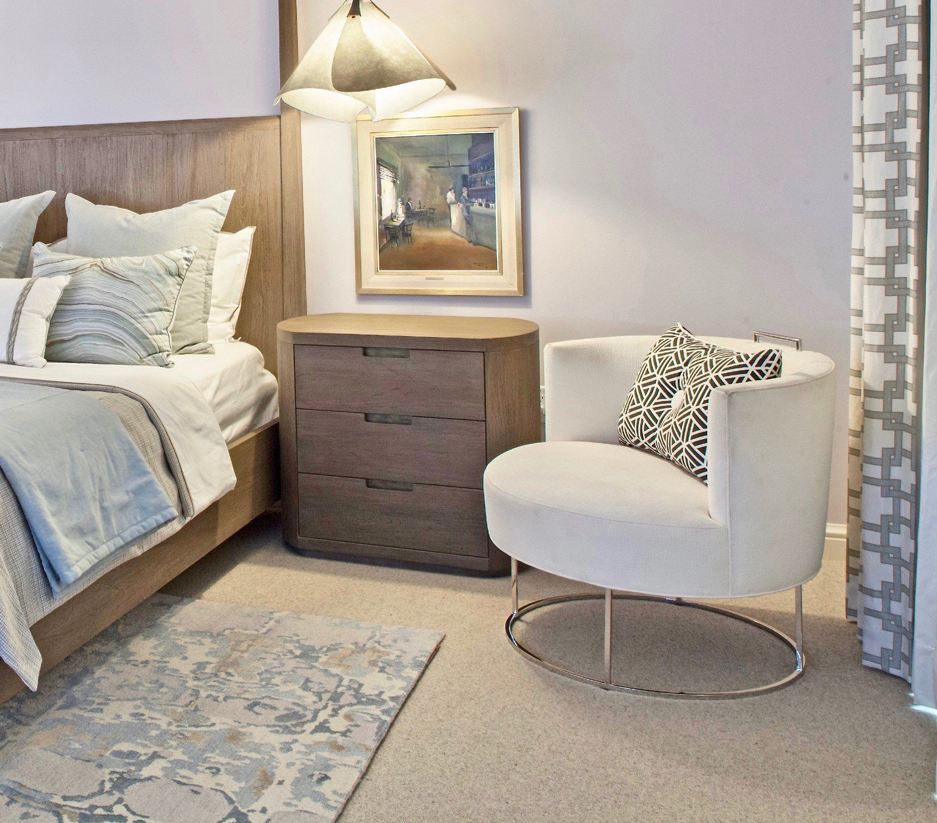 Cozy bedroom corner with bed, dresser, lamp, round chair, and patterned rug in neutral tones
