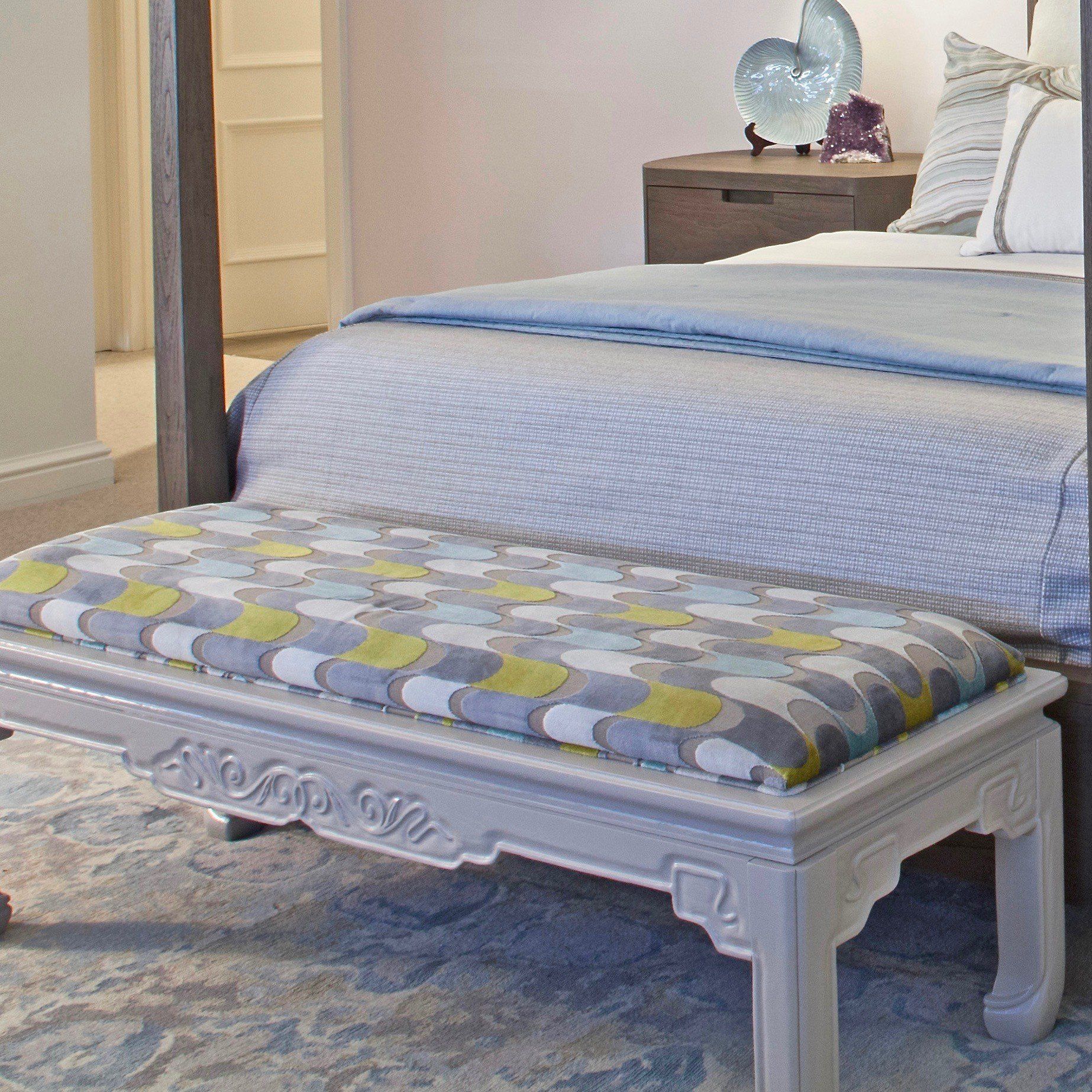Decorative upholstered bench at the foot of a blue bed in a softly lit bedroom