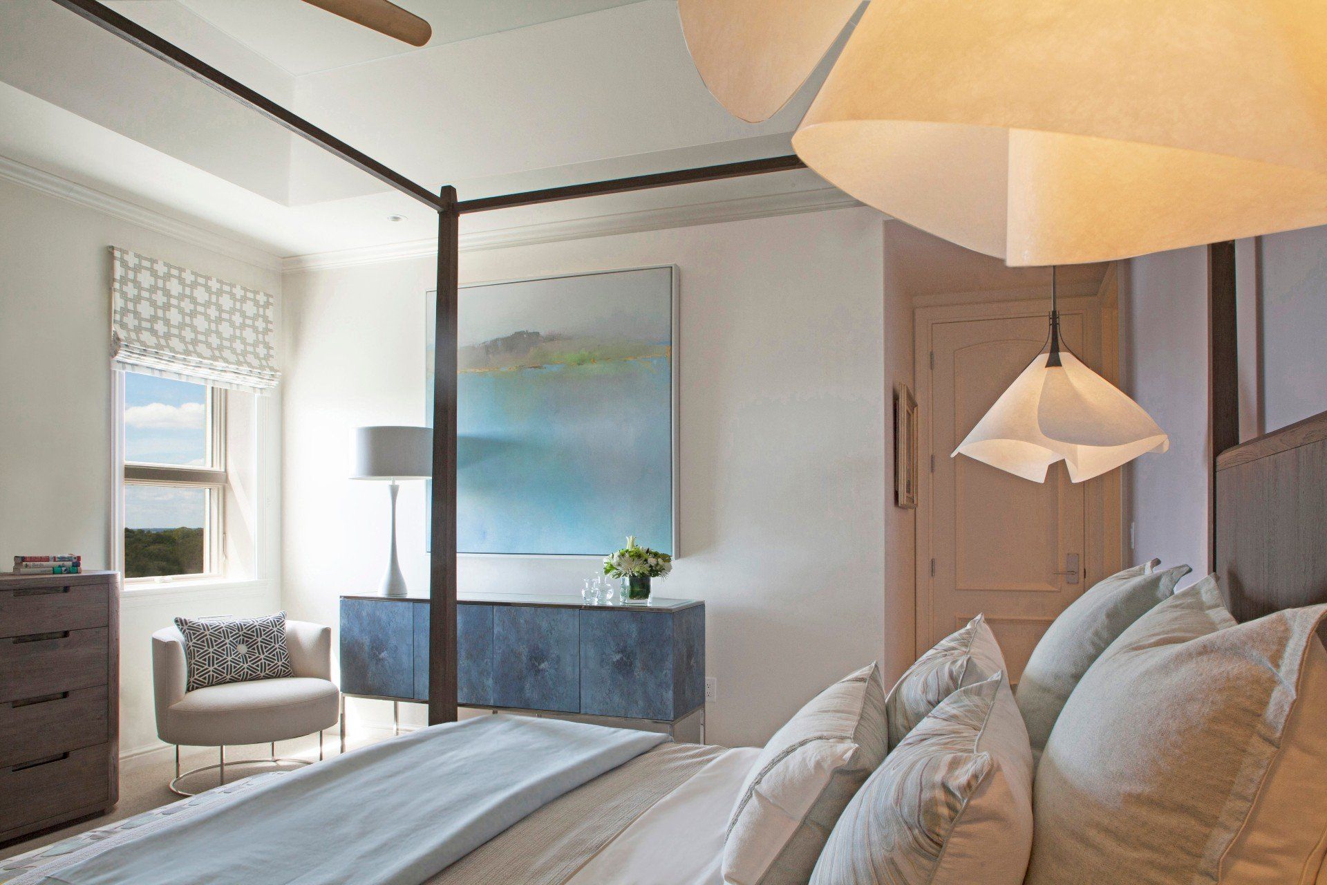 Bright bedroom with white bedding, blue dresser, window seat, and soft pendant lighting